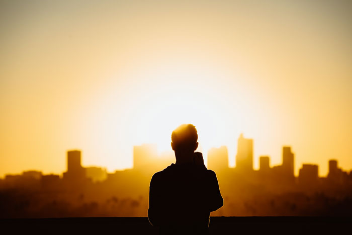 Picture of man silhouette at sunrise and city in the background
