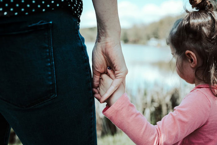 Adult and child holding hands near a lake, evoking mysterious vibes linked to children's imaginary friends stories.
