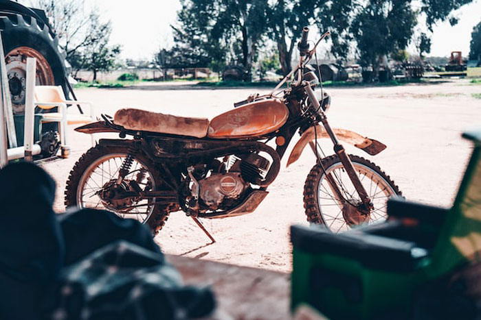 Rusty old dirt bike parked outside in a sunny yard, invoking creepy stories about children's imaginary friends and eerie memories.