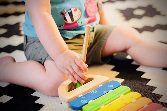 Child playing with colorful wooden toy on patterned rug, evoking creepy stories about children's imaginary friends.