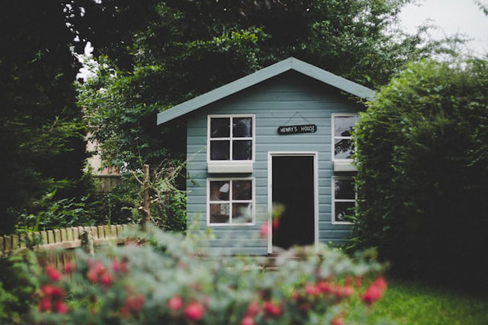 Small blue playhouse named Henry's House in a garden surrounded by greenery, evoking creepy children's imaginary friends stories.
