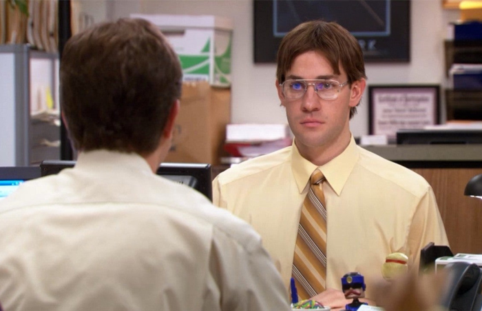 Man in a yellow shirt and tie sitting at office desk facing another person, illustrating fake friend and toxic relationship signs.