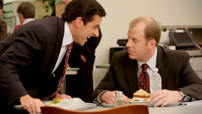 Two men in suits having a tense lunch conversation, illustrating signs of a fake friend and a toxic relationship.