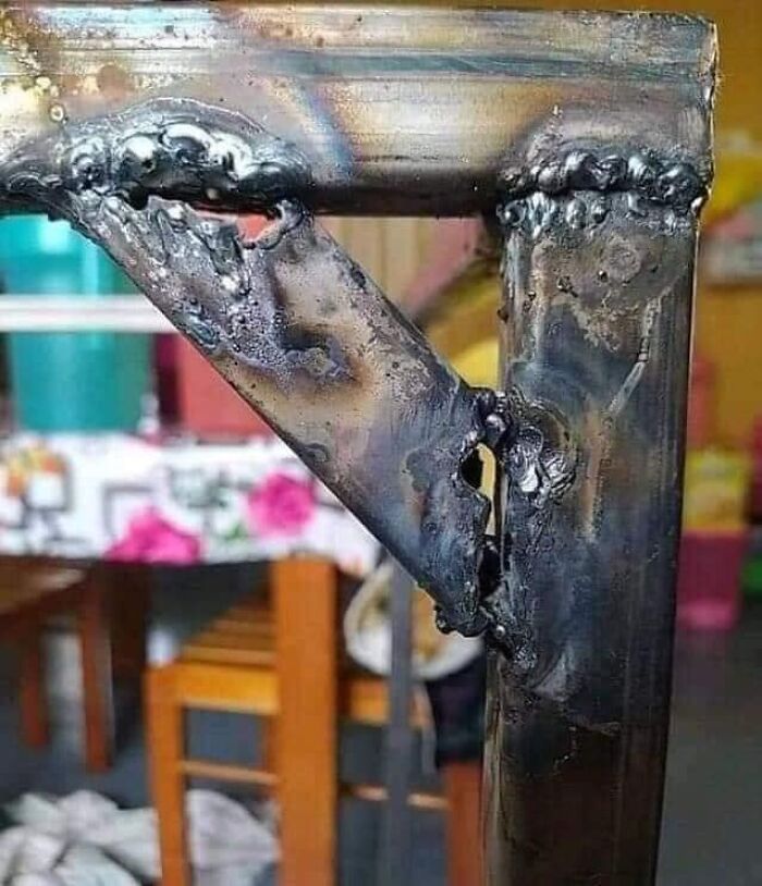 Poorly welded metal joint, lacking OSHA safety compliance, in a casual setting with a colorful tablecloth and wooden chairs.