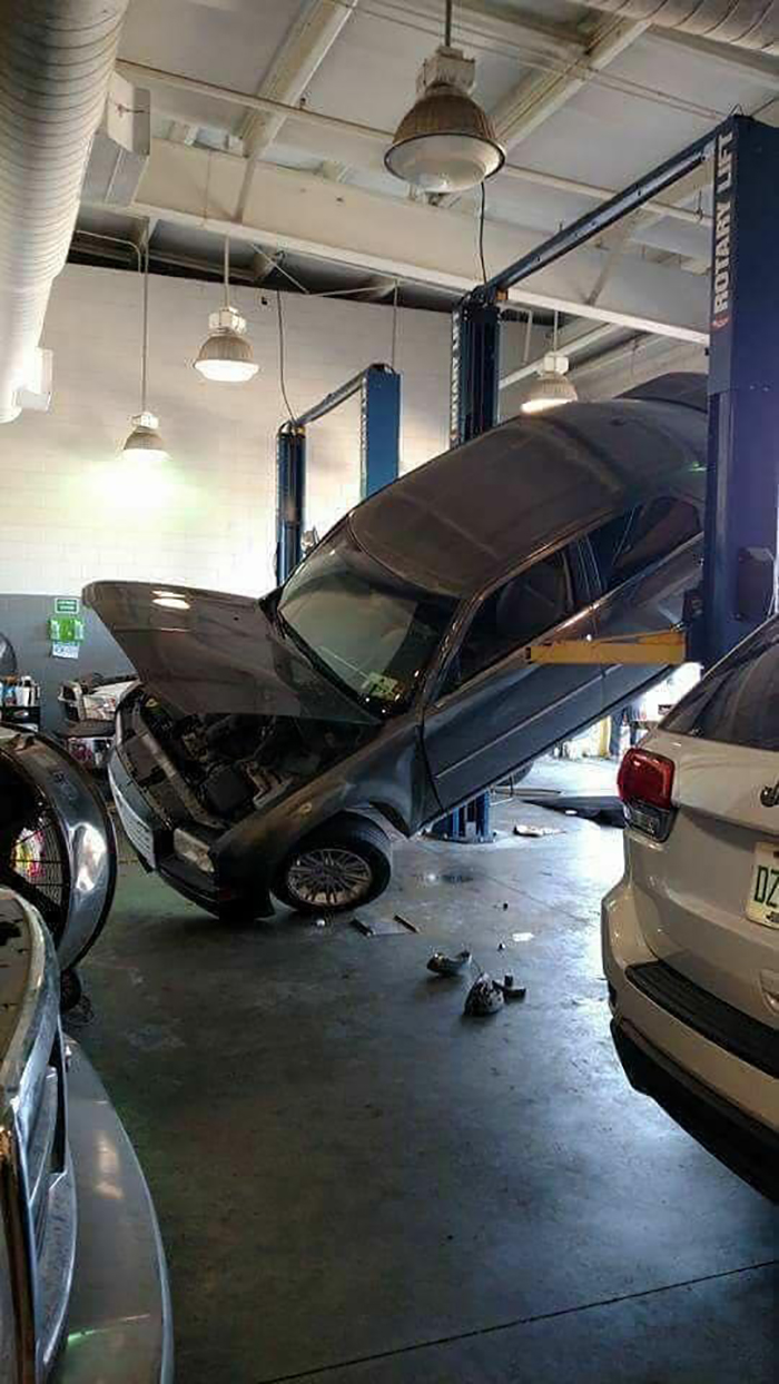 Car precariously tilted on a lift in a garage, disregarding OSHA safety regulations.