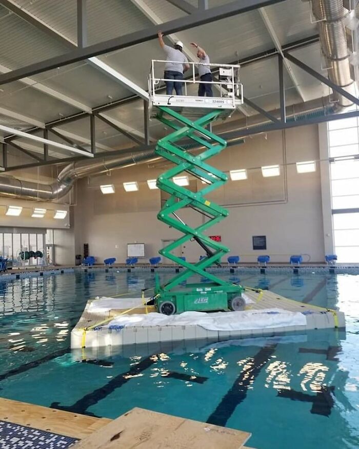 Two workers on a scissor lift above a pool, highlighting questionable OSHA safety practices.
