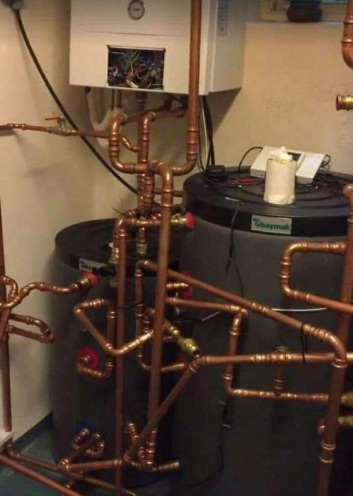 Complex plumbing system with exposed pipes and wires, appearing to disregard OSHA safety regulations.