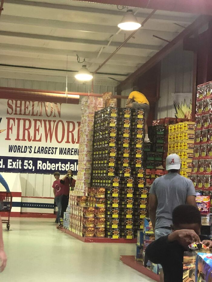 Person climbing stacked boxes in a fireworks warehouse, disregarding OSHA safety regulations.