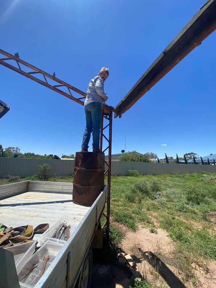 Person balancing on barrels atop a truck, disregarding OSHA safety regulations.