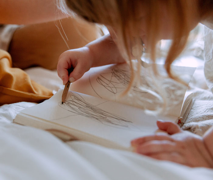 Child drawing with pencil in a notebook, exploring creativity and curious facts about art not taught in classes.