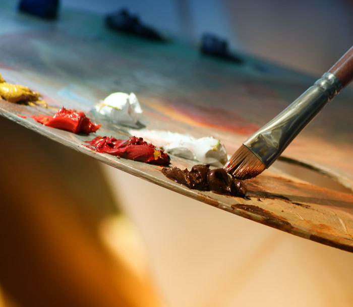 Brush touching brown paint on a palette with various colors, illustrating curious facts about art techniques and classes.