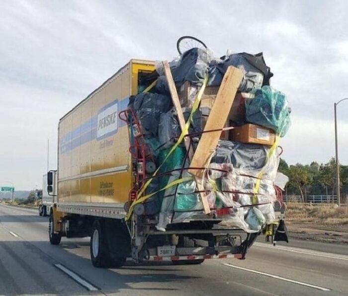 Overloaded truck defying OSHA safety standards on highway, cargo secured with straps.