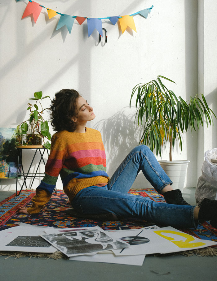 Young woman relaxing on carpet with drawings around her, immersed in curious art facts and creative inspiration.