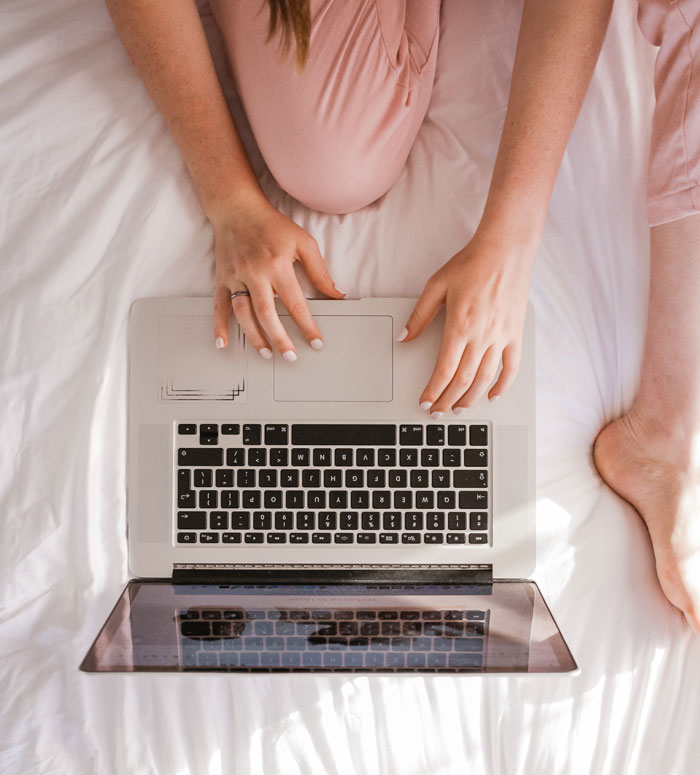 Woman sitting on a bed and typing on the laptop