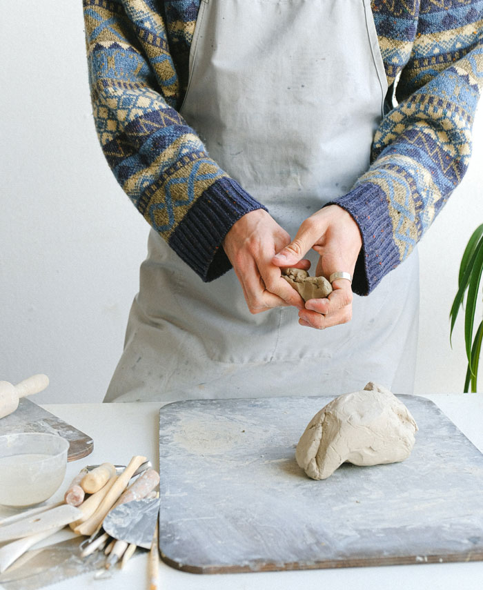 Man in a sweater and apron sculpting clay, demonstrating curious facts about art techniques not taught in classes.