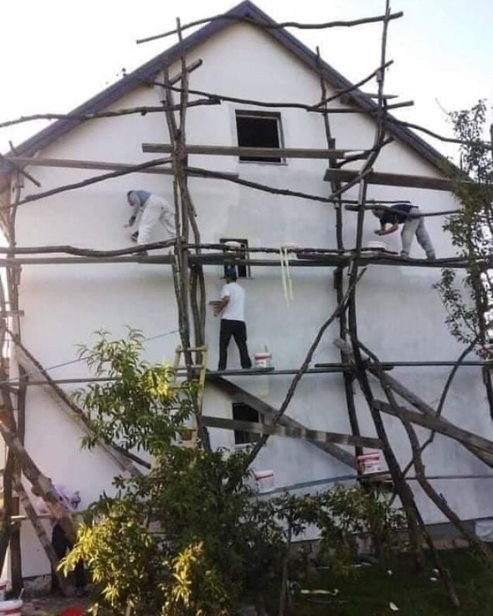 Unsafe scaffolding setup with workers on a house, ignoring OSHA safety regulations.