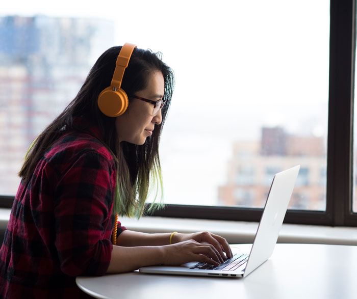Woman with yellow headphones on typing on the laptop 