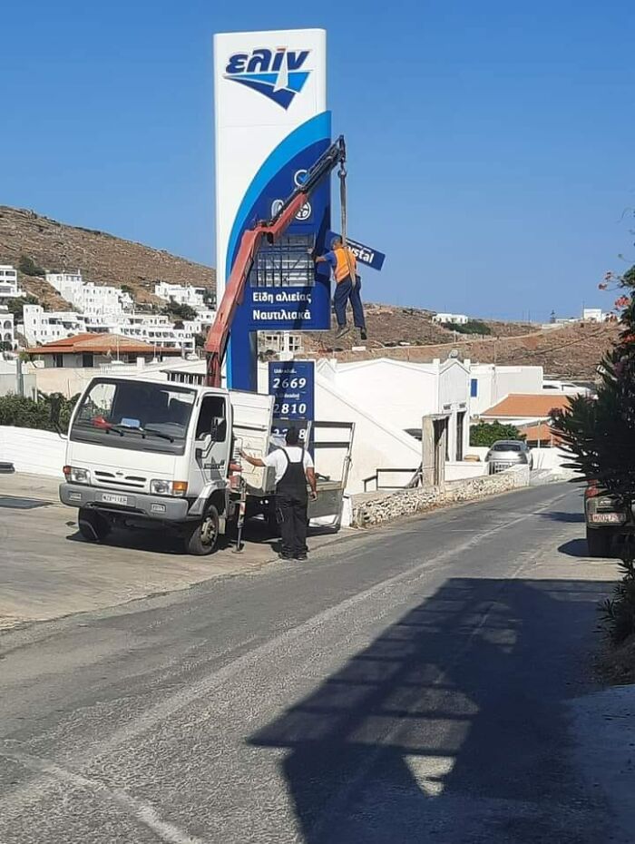 Worker on crane lift fixing sign, ignoring OSHA safety regulations.