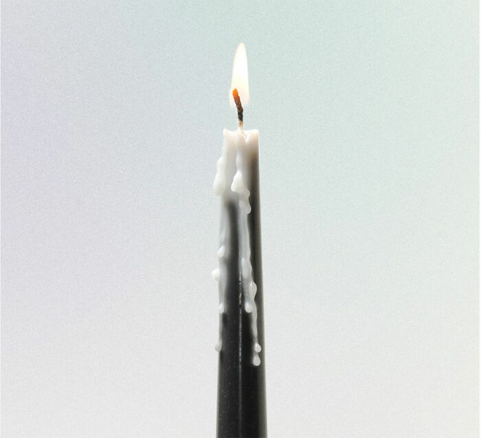 Black candle with white wax drips burning at the wick, showcasing an unusual and conceptual product design reflection.