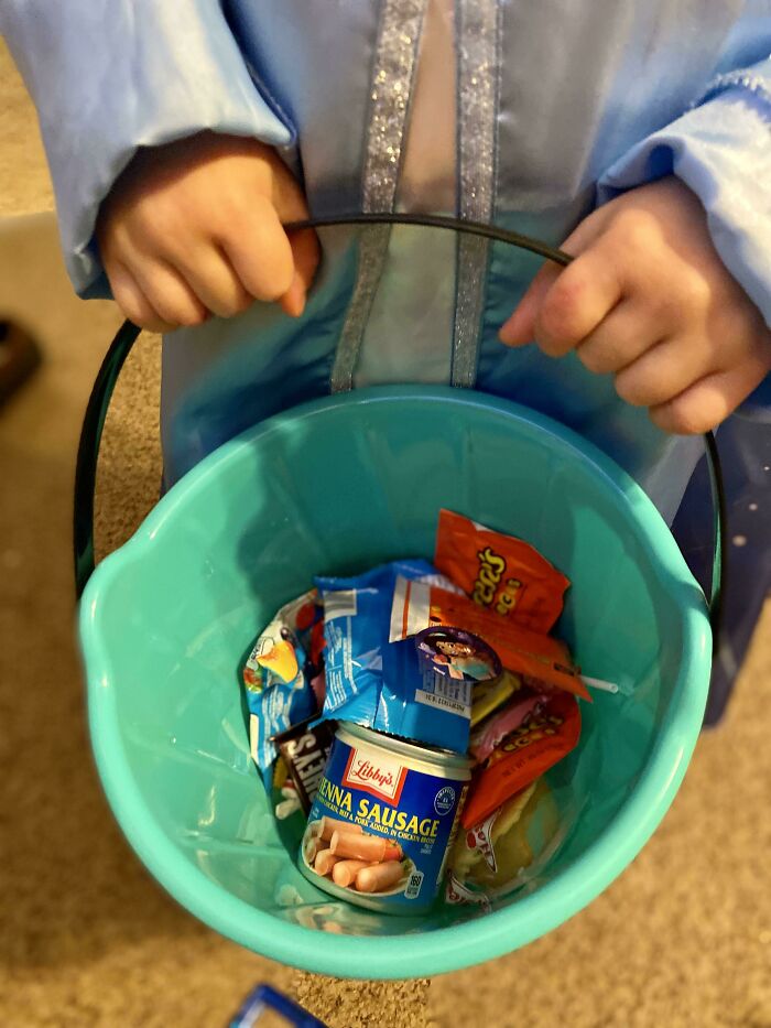 Child holding a Halloween bucket filled with candy and a can of Vienna sausage, showing funny Halloween moments kids made parents laugh.