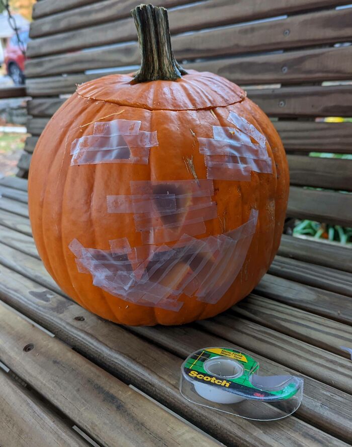 Pumpkin with a taped smiley face on a wooden bench, showing kids' Halloween creativity that made parents laugh hard.