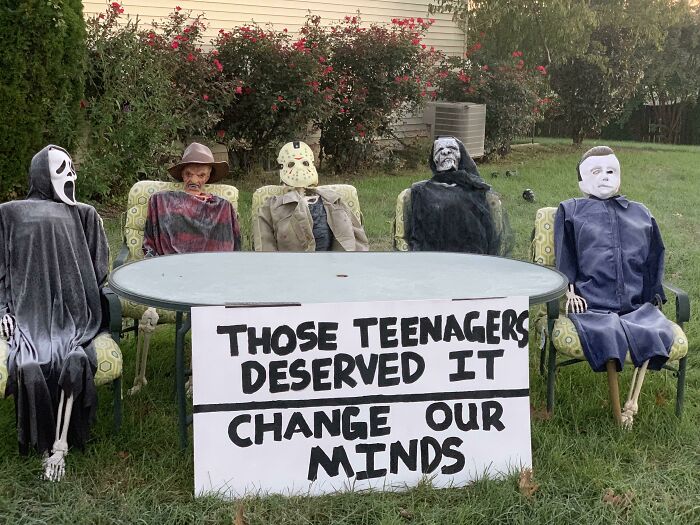 Halloween decorations with spooky figures sitting around a table holding a funny sign about teenagers making parents laugh.