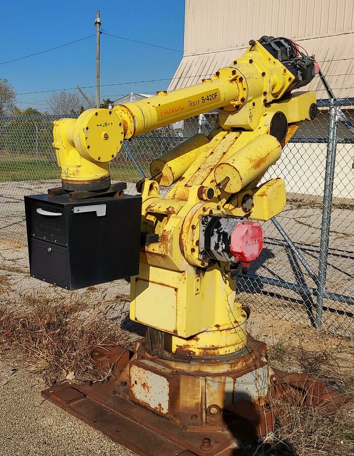 Yellow industrial robotic arm holding a black mailbox, showcasing one of the most creative and cool mailboxes spotted.