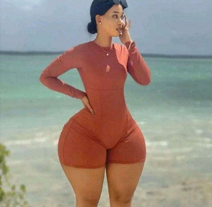Woman wearing a tight rust-colored bodysuit posing on the beach with exaggerated edited hips in Instagram reality photo.