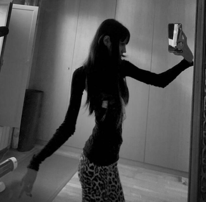 Person taking a mirror selfie with a distorted selfie pose showing an unnaturally thin arm and waist, Instagram reality.