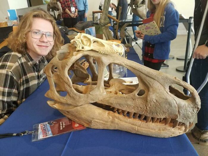 Person smiling next to a large dinosaur skull fossil, showcasing nature was metal with powerful prehistoric bones.