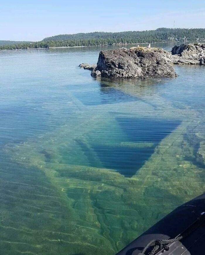 Sunken shipwreck visible underwater near rocky shore in a clear ocean, evoking frightening ocean images to avoid.