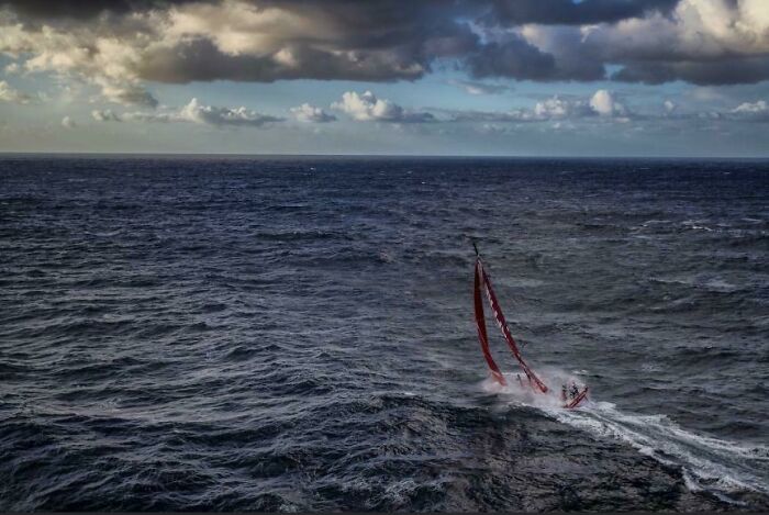 Small sailboat struggling in rough ocean waves under a dramatic cloudy sky, evoking frightening ocean scenes.