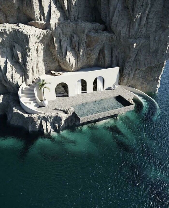 Modern white villa with pool built into rocky cliffside overlooking deep, dark ocean water in a remote coastal location.