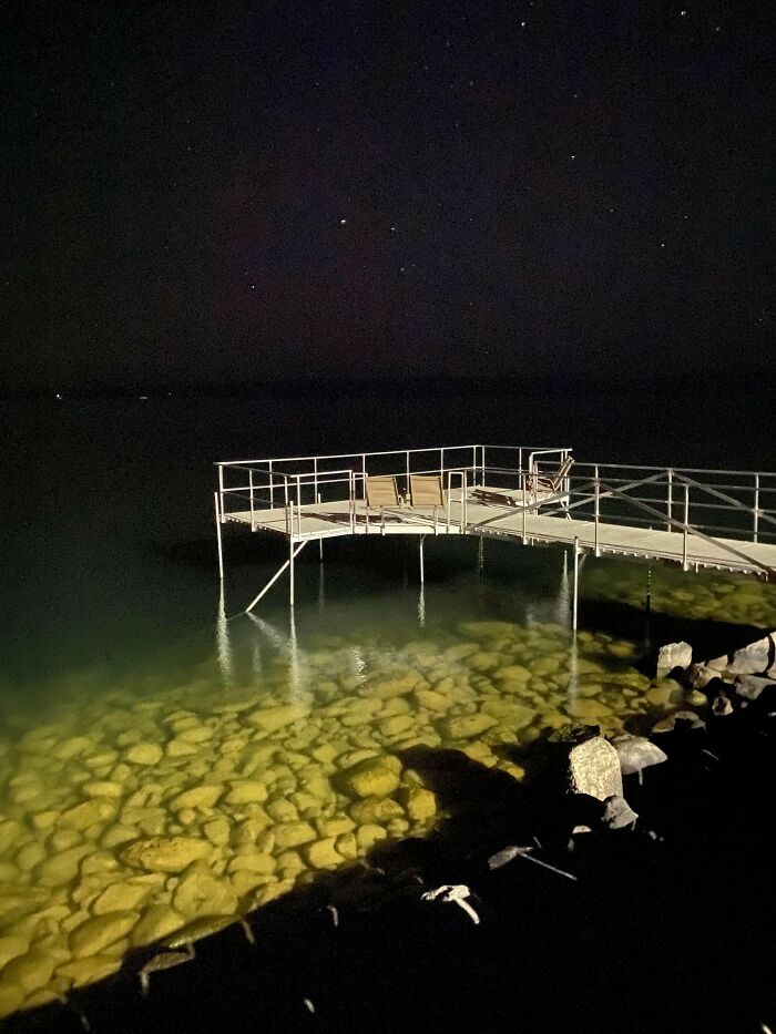 Night view of a rocky ocean shore with a metal dock extending over eerie shallow water in a frightening ocean scene.