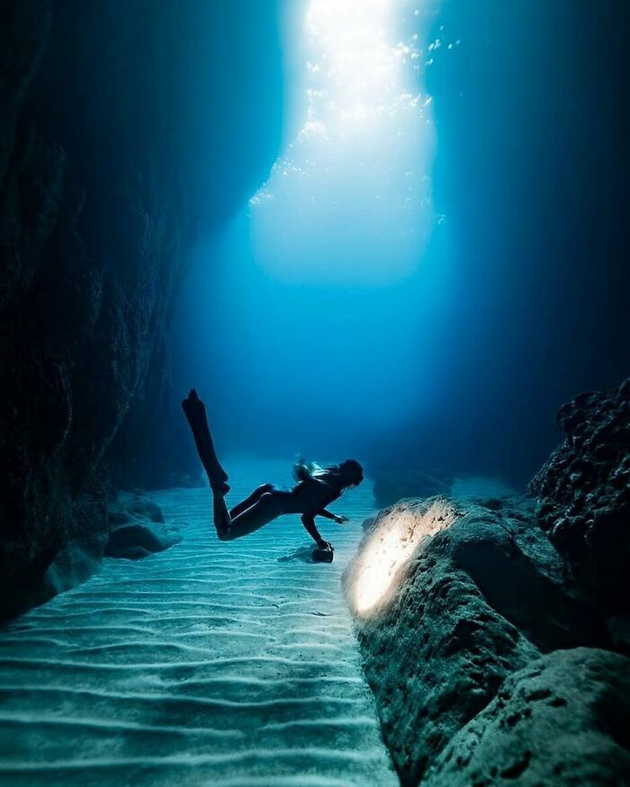 Underwater scene with a diver exploring a deep ocean cave illuminated by natural light from above.