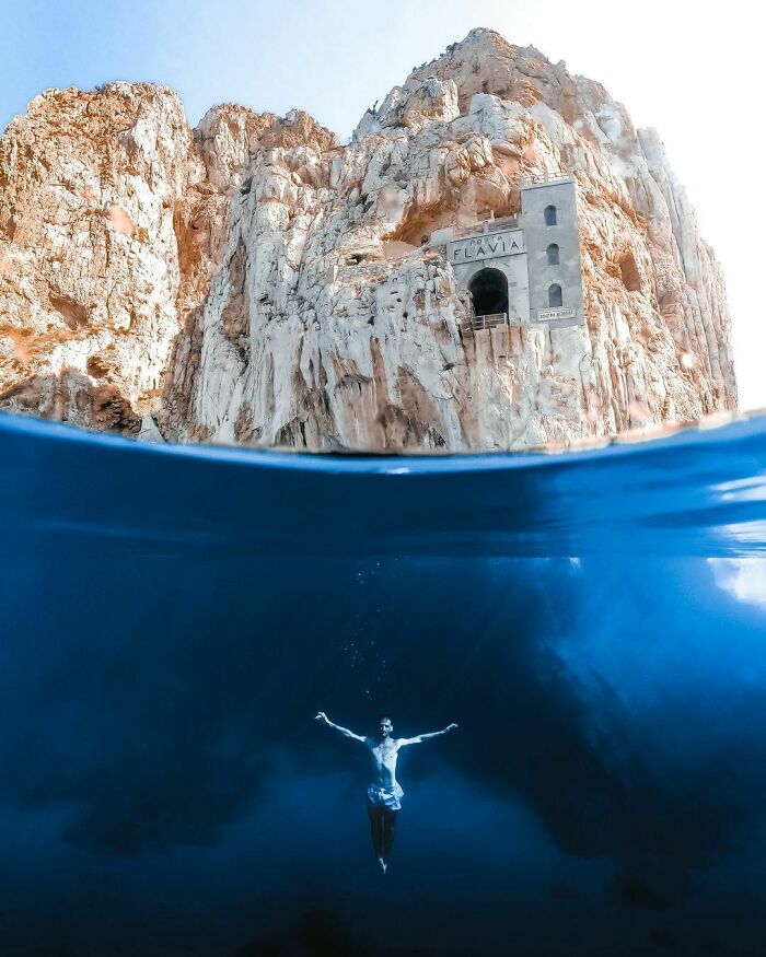 Underwater view of a swimmer near rocky cliffs and an ancient stone structure by the ocean, evoking a frightening ocean scene.
