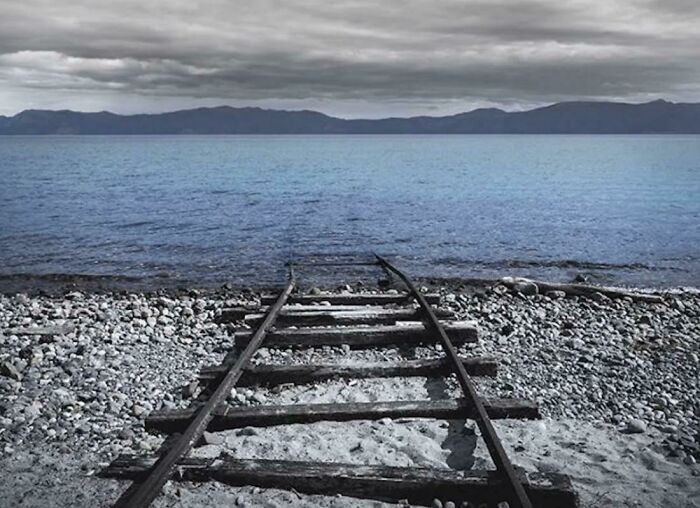 Abandoned railway tracks leading into the ocean under a gloomy sky in a frightening ocean scene.
