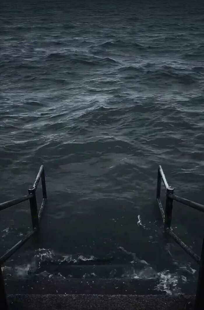 Dark ocean waves crashing against metal stairs leading into the water, evoking frightening ocean fears.