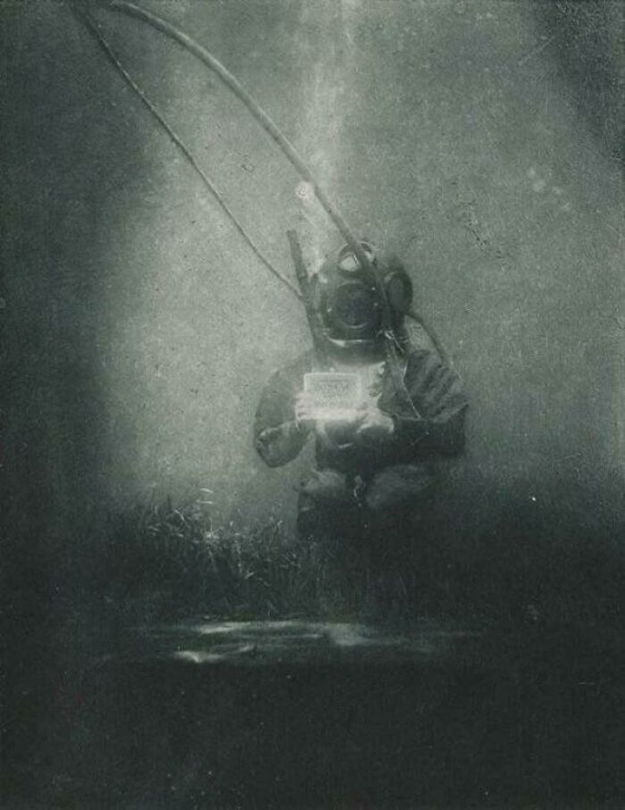 Underwater diver in vintage suit holding device, surrounded by murky water in a frightening ocean scene.