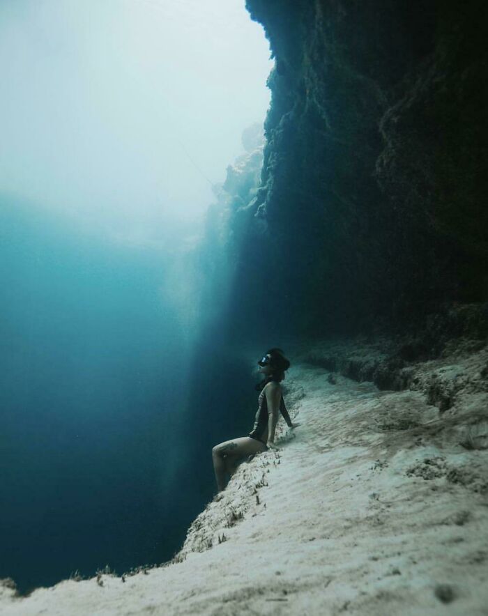 Diver sitting on the edge of a deep underwater cliff in the ocean, highlighting frightening ocean depths.