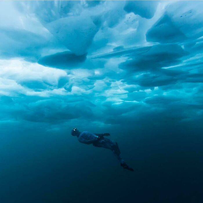 Diver swimming under dark ocean ice with ominous blue tones, evoking frightening ocean scenes that warn of danger.