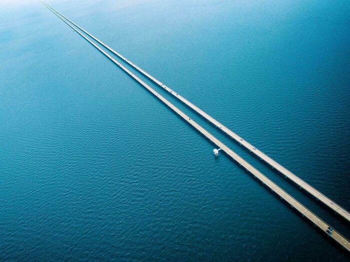 Aerial view of a long, narrow bridge stretching over the ocean, highlighting vast, open water and minimal traffic.