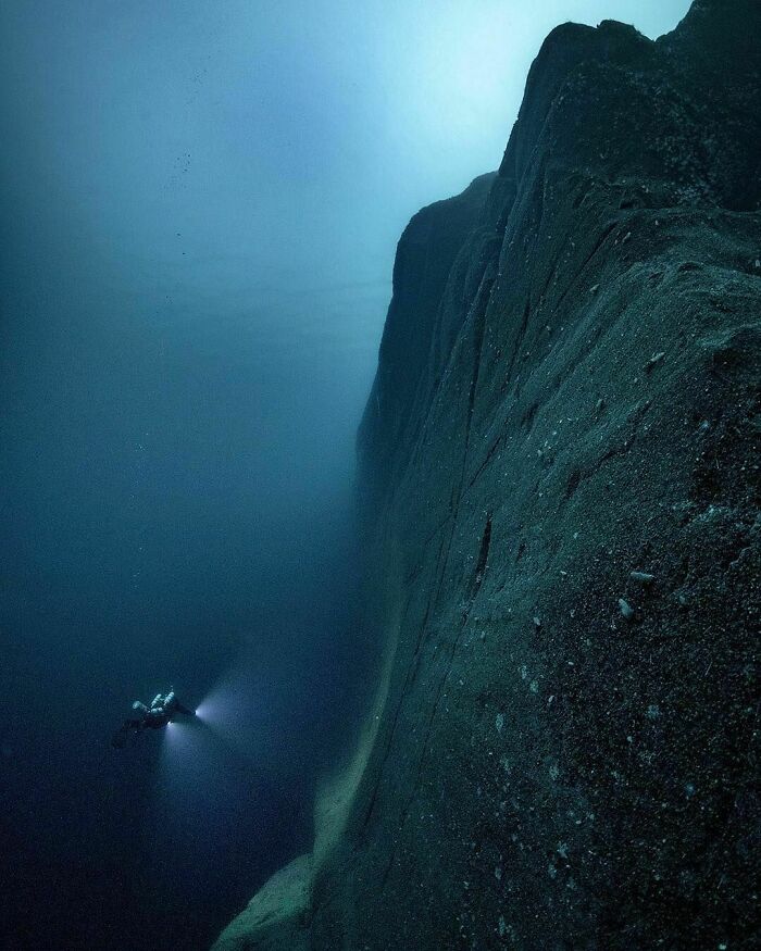 Deep ocean cliff with a diver exploring the dark and eerie underwater abyss, highlighting frightening ocean scenes.