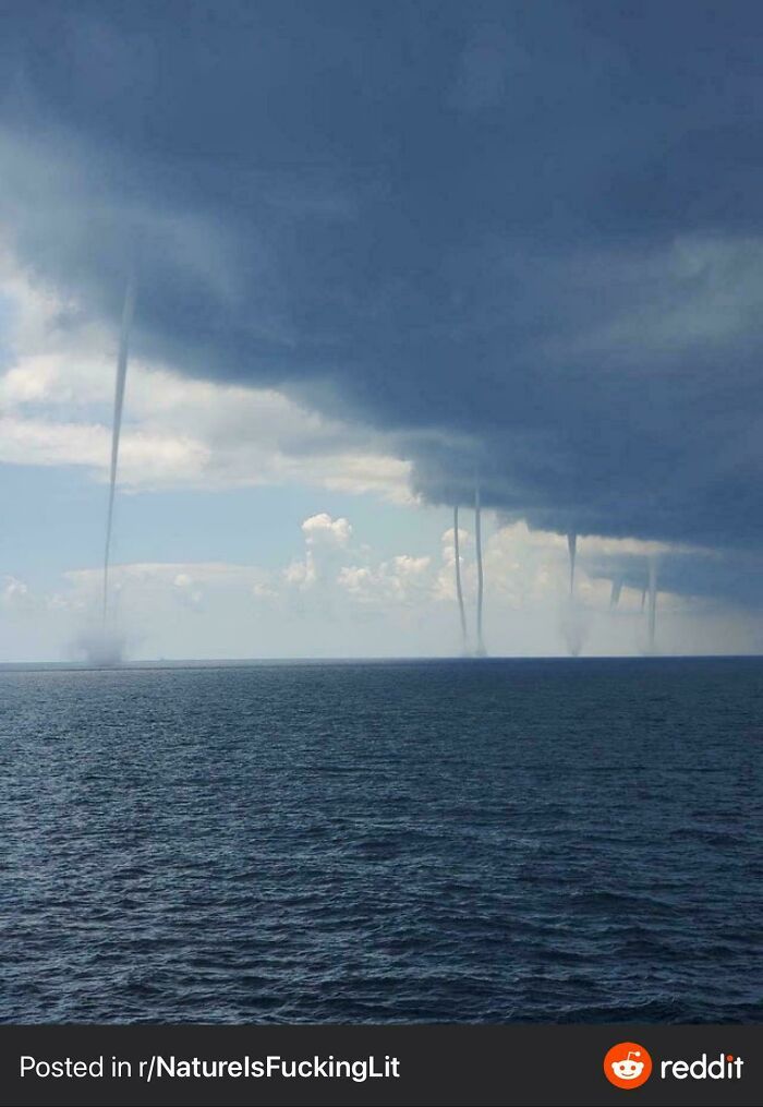 Multiple waterspouts forming over the ocean under dark storm clouds, creating a frightening natural ocean scene.