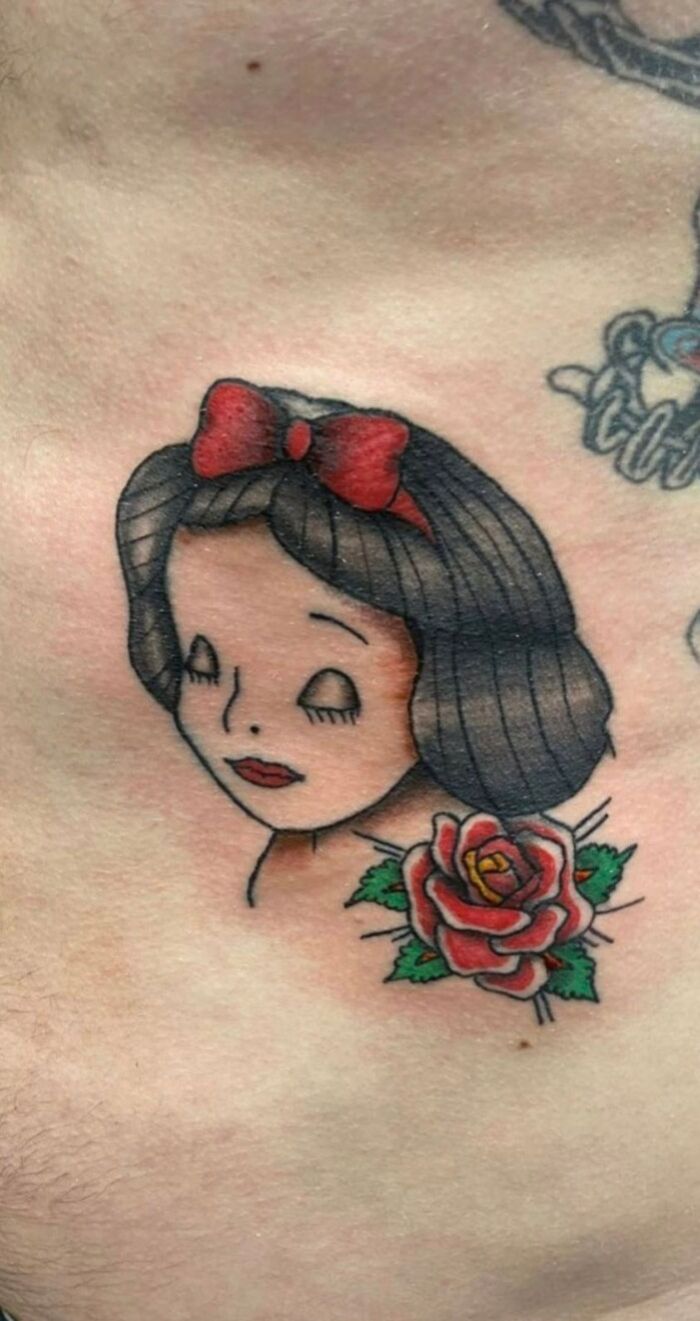 Tattoo of a girl with a red bow and a red rose underneath, showcasing bad tattoo art.
