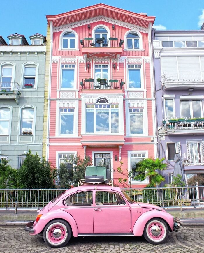 Pink vintage car parked in front of a colorful architect-designed building with intricate details and balconies.