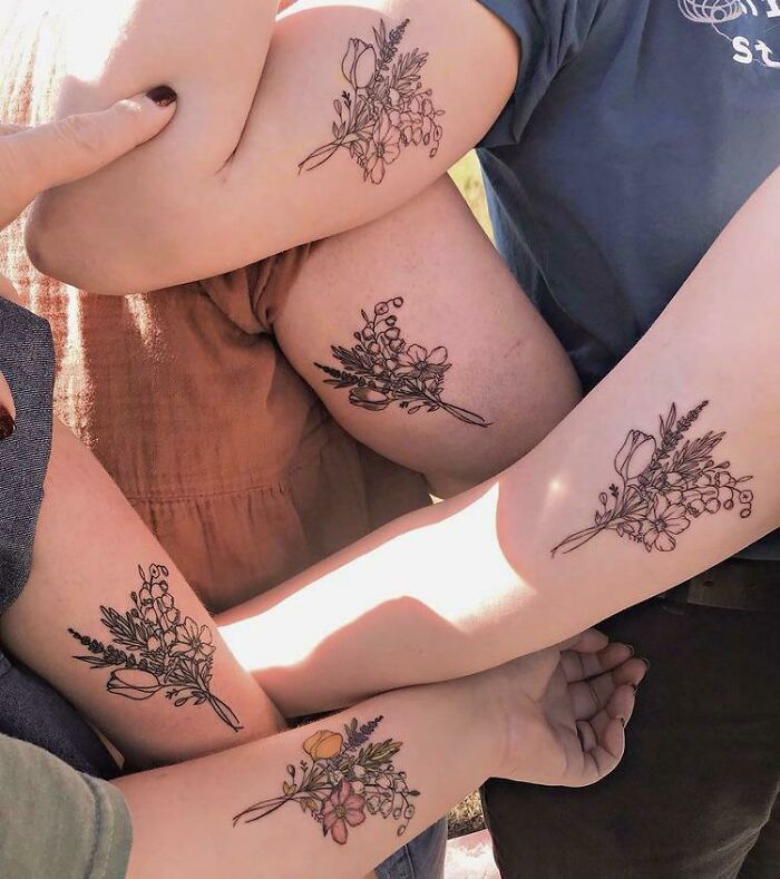 Four arms with matching floral best friend tattoos symbolizing friendship.