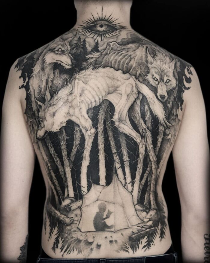 Back tattoo design featuring wolves and forest scene with an eye above.