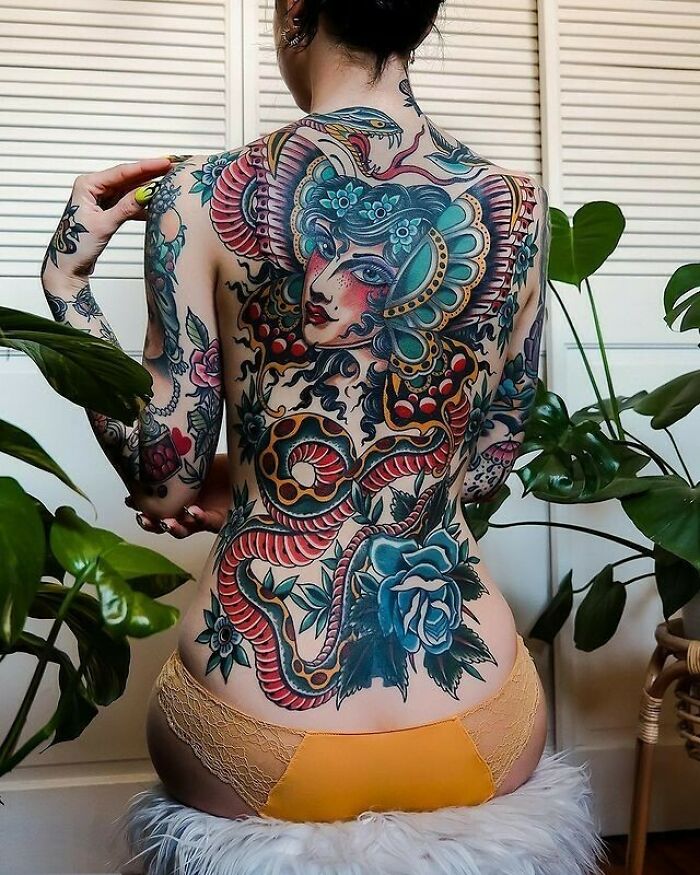 Intricate back tattoo design featuring a colorful snake and woman's face in a floral motif, showcasing creative tattoo art.