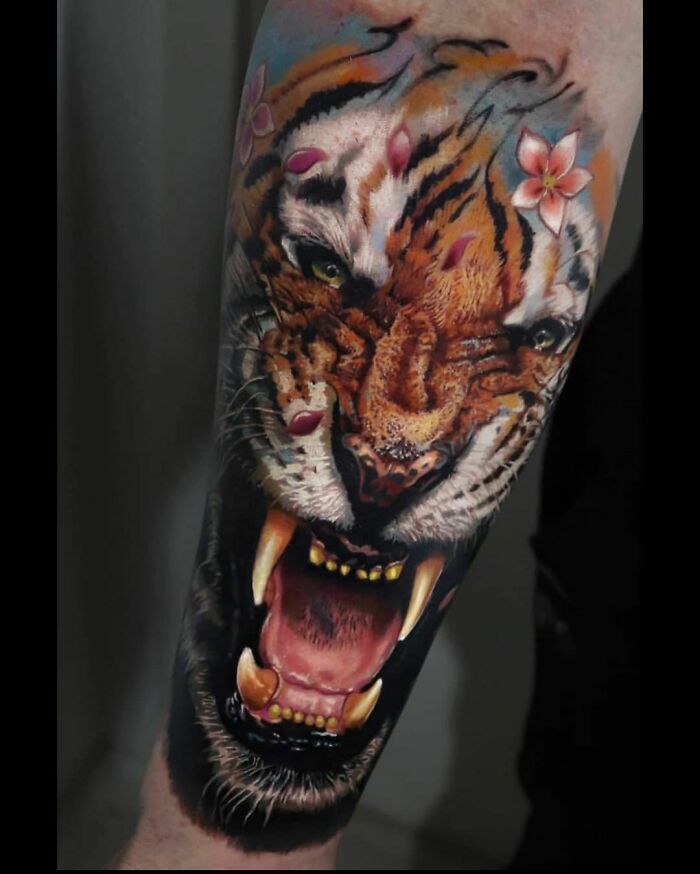 Tiger tattoo design featuring vibrant colors and floral accents on an arm, showcasing artistic creativity.